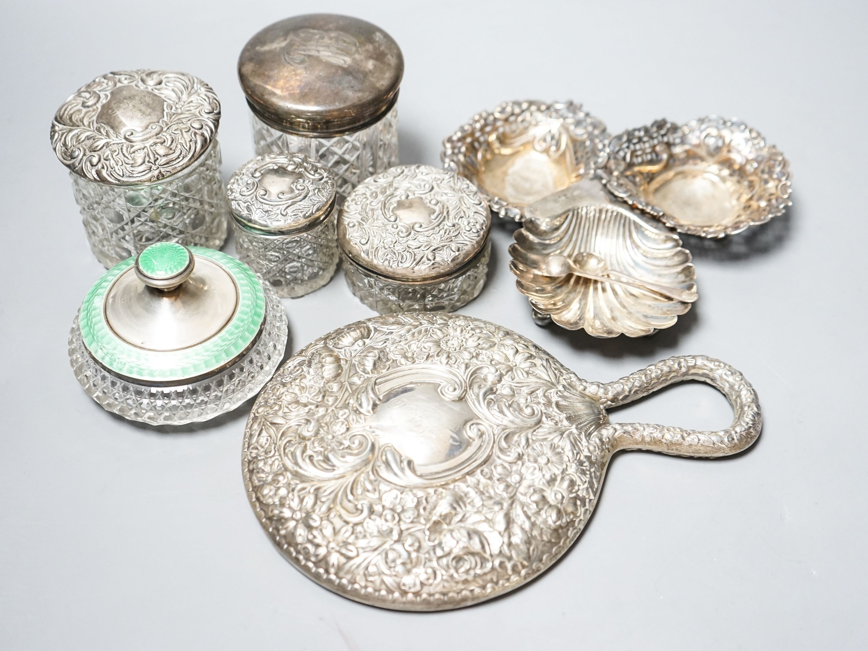 A silver and enamel mounted glass toilet jar, four other toilet jars, a hand mirror and three small silver dishes.